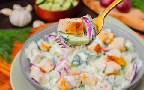 Ein Löffel mit einem Stück Hähnchen, Gurke und roter Zwiebel, bereit, in einen cremigen Salat zu tauchen. Perfekt für proteinreiche Salate!