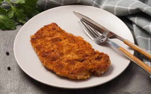 Kotlet schabowy w panierce na talerzu z widelcem i nożem.