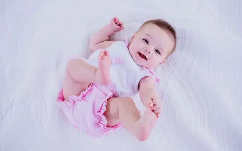 Bebé sonriente con un traje rosa y blanco, perfecto para inspirar nombres de niñas.