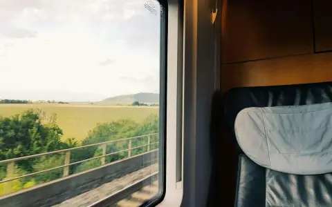 Blick aus dem Zugfenster auf grüne Felder und Hügel. Bequemer Sitzplatz im Abteil, bereit für die Reise durch den Euro city.