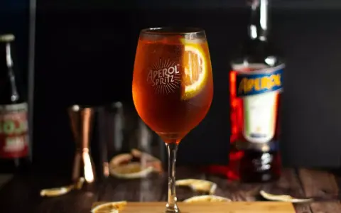 Orzeźwiający Aperol Spritz z plastrem pomarańczy, obok butelki Aperolu. Poznaj różne rodzaje Aperolu i jego zastosowania.