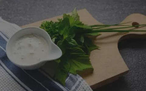 Sauce tartare maison crémeuse dans un ramequin blanc, accompagnée d'herbes fraîches sur une planche en bois.