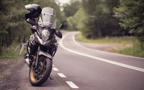 Moto pronta per avventurosi itinerari in moto su una strada tortuosa tra alberi. Casco appoggiato sul manubrio.
