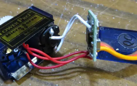 Ein Tower Pro Micro Servo mit Zahnrädern und einem 1m Verlängerungskabel, verbunden über eine kleine Platine.