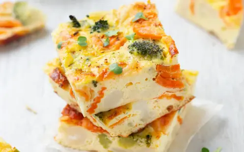 Fette di frittata al forno con verdure, broccoli e carote, guarnita con germogli freschi. Un piatto colorato e salutare.