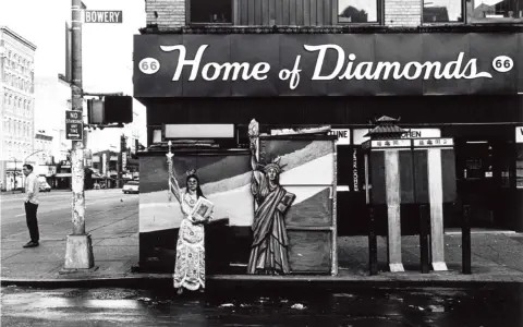 Corky Lee photos: A person in ornate robes stands beside a Statue of Liberty cutout on a wet street, with "Home of Diamonds" sign above.