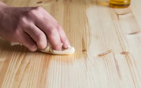 Main d'artisan essuyant un bois fraîchement poncé avec un chiffon humide pour le nettoyer.