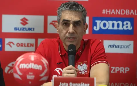 Jota González, trener reprezentacji Polski w piłce ręcznej, przemawia do mikrofonu. Obok niego czerwona piłka.