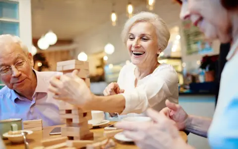 Anziani ridono giocando a Jenga, un esempio di iniziative per anziani che promuovono divertimento e socialità.