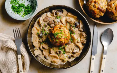 Herzhaftes Gericht: Ein Knödel in cremiger Pilzrahmsoße, garniert mit Schnittlauch. Perfekt, was passt zu Brezenknödel!