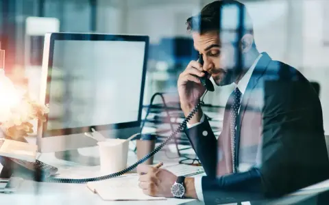 Biznesmen w garniturze rozmawia przez telefon, notując w zeszycie. Nawet w obliczu siły wyższej, praca wre.
