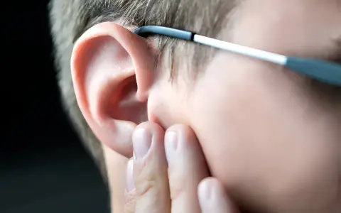 Dłoń dotyka ucha, sugerując uczucie zatkanego ucha. Okulary opierają się o skroń.