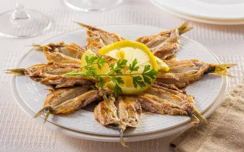 Piatto di alici alla scapece disposte a raggiera, guarnite con fette di limone e prezzemolo.