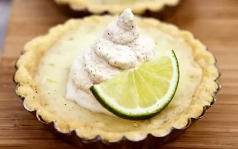 En liten key lime pie med en virvel av gräddig topping och en limeklyfta.