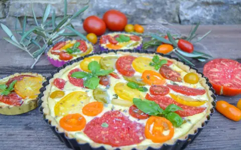 Eine herzhafte Tomaten Quiche mit bunten Tomatenscheiben und frischem Basilikum, garniert mit Lavendelblüten.