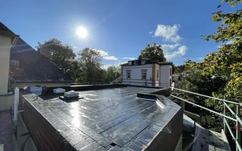 Ein frisch abgedichtetes Flachdach unter strahlender Sonne. Die Dachhaut glänzt, zwei Dachfenster sind sichtbar.