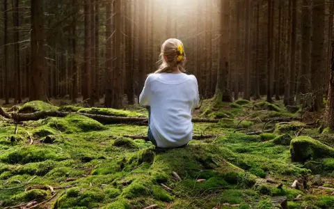 Frau sitzt im Wald auf moosbewachsenem Boden, sucht Ruhe, wenn sie immer gestresst und genervt ist.