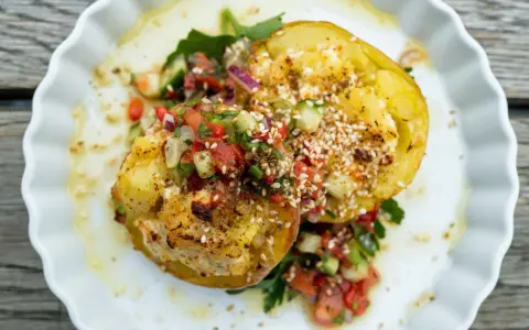Kumpir rezept: Zwei gebackene Kartoffelhälften, gefüllt mit Käse und belegt mit frischem Tomaten-Gurken-Salat und Sesam.