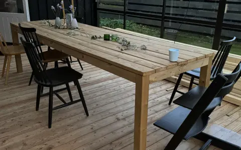 Ett träbord och stolar på en altan. Bordet är dekorerat med blommor och ljus. Perfekt för att behandla furu utomhus och njuta av sommaren.