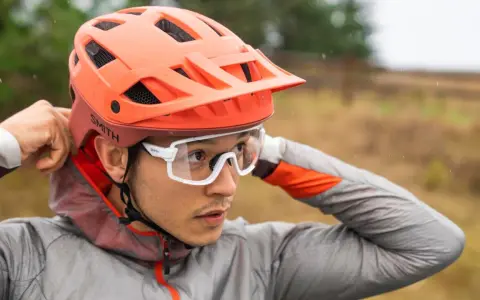 Uomo con casco da bici arancione e occhiali bianchi, mentre regola il casco. Utile per capire come misurare la testa per il casco.