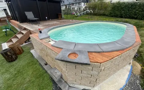 Ein Pool mit selbstgemachten Randsteinen, umgeben von Holz und Naturstein.