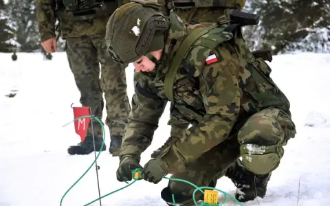 Żołnierz w zimowym kamuflażu, kto to saper, ostrożnie pracuje z przewodami i flagą z literą "M".