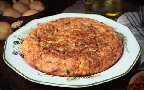 Tortilla española, un clásico de la comida típica de Granada, servida en un plato decorado. Patatas y aceite en el fondo.