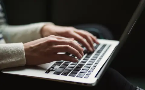Dłonie piszą na laptopie. Ktoś przygotowuje wypowiedzenie umowy o pracę po angielsku, szukając wzoru.