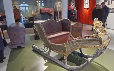 Złota, zdobiona sanie w muzeum tradycji szlacheckiej w Waplewie Wielkim. Obok skrzynie.