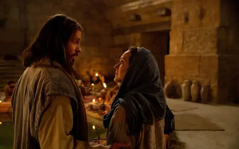 Scena z Kany Galilejskiej: Jezus rozmawia z kobietą, w tle widać gości weselnych i świece.