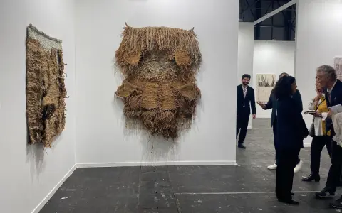 Exposición de arte contemporáneo con tapices texturizados y personas observando.