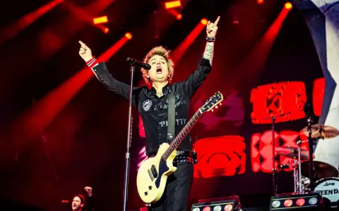 Billie Joe Armstrong, en av medlemmar av Green Day, sjunger och spelar gitarr på scenen under en konsert, upplyst av röda strålkastare.