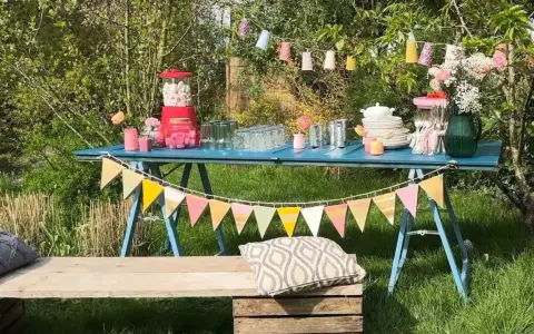Une table bleue dressée pour une deco garden party à faire soi même, avec guirlandes, bonbons et fleurs.