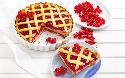 Pyszna tarta z porzeczkami, z kratką z ciasta i świeżymi owocami na wierzchu. Obok kawałek ciasta na talerzyku.