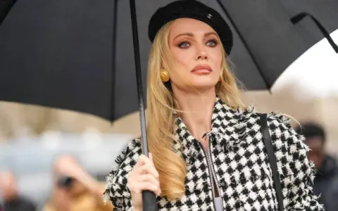 Mujer con boina negra y chaqueta a cuadros, sosteniendo un paraguas. Su maquillaje es un perfecto ejemplo de soft glam.