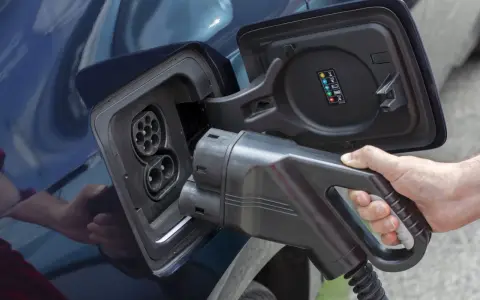 Mano insertando cargador en coche eléctrico. Averigua cuanto tarda en cargar un coche eléctrico en casa.