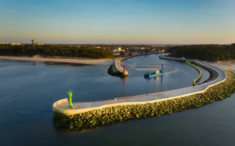 Port w Mrzeżynie z falochronami i latarniami morskimi. Widoczna łódź pogłębiarka. Mrzeżyno atrakcje dla miłośników morza.