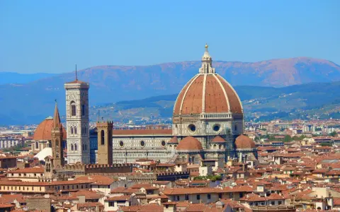 Vue panoramique de Florence avec le **dôme de Brunelleschi** dominant la ville, sous un ciel bleu clair.
