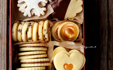 Scatola piena di biscotti al burro: fiocchi di neve, con gocce di cioccolato, ripieni di caramello e a forma di cuore.