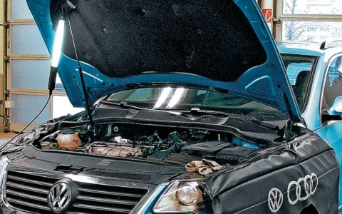 Pod maską niebieskiego VW z silnikiem 2.0 TDI, mechanik oświetla silnik lampą.