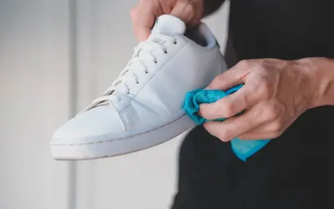 Mani che puliscono una scarpa bianca Adidas Stan Smith con un panno blu. Ecco come lavare le Stan Smith per farle tornare come nuove.