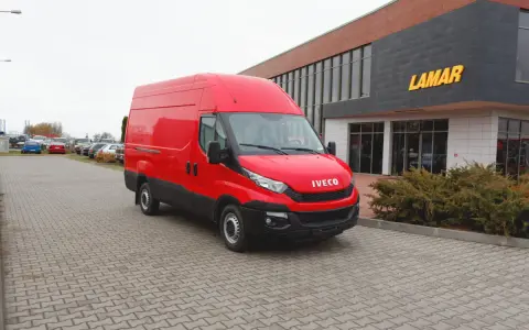 Czerwony bus Iveco na parkingu przed budynkiem z napisem LAMAR.