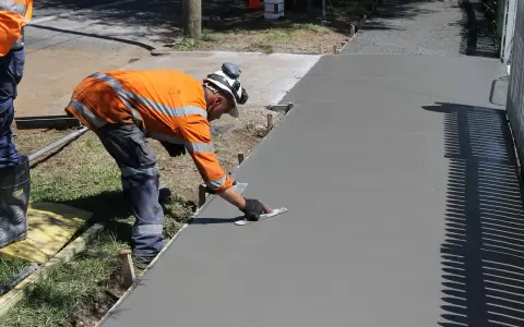 Robotnik wygładza świeży beton, zastanawiając się, ile kosztuje kubik betonu na nową ścieżkę.