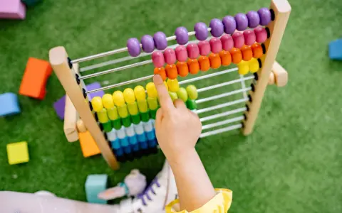 Dziecko ćwiczy dodawanie do 10, przesuwając kolorowe koraliki na liczydle.