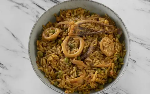 Un delicioso plato de arroz con calamares y guisantes, servido en un cuenco sobre una superficie de mármol.