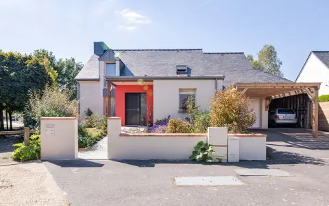 Maison moderne avec entrée rouge vif et carport en bois. Idéal pour estimer le prix rénovation maison m2.