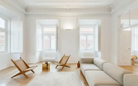 Ecco cosa fa l'architetto d'interni: crea un soggiorno minimalista con divano chiaro, sedie in legno e un tavolino dorato, valorizzando la luce naturale.