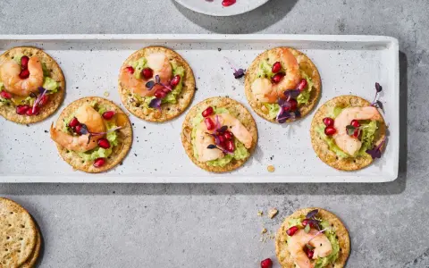 Mediterranes Fingerfood kalt: Garnelen auf Avocado-Creme mit Granatapfelkernen und Kräutern auf Crackern.