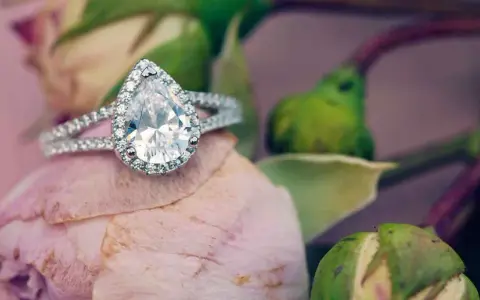 Un prezioso anello a goccia, simbolo di purezza e amore eterno, adagiato su un petalo di rosa.