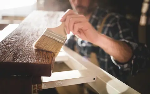 Carpintero aplicando barniz a madera, mostrando la diferencia entre laca y barniz.